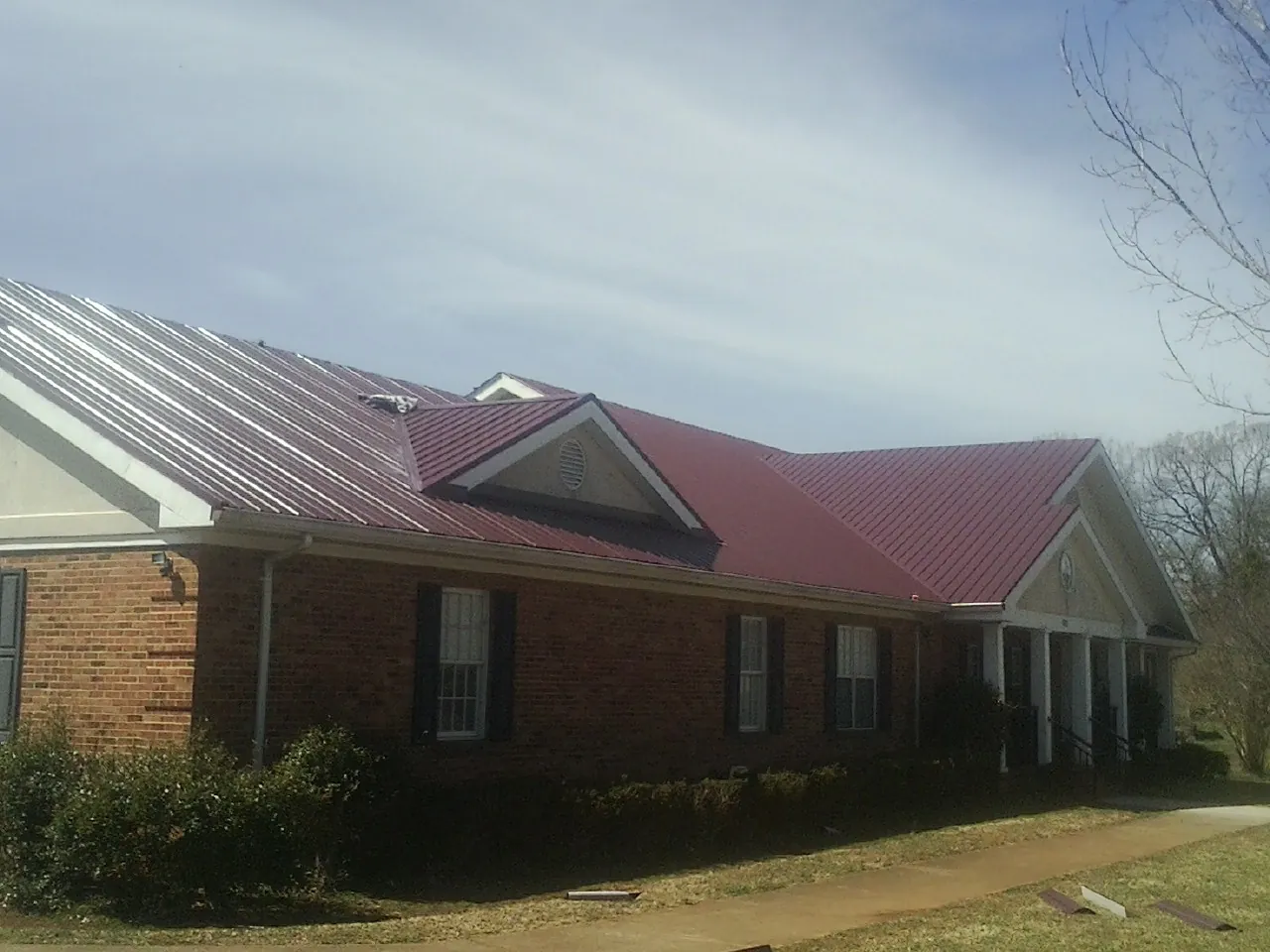 Red metal roof with gabled entries on a long brick building, from a Hail Damage Roof Repair job in Brodhead