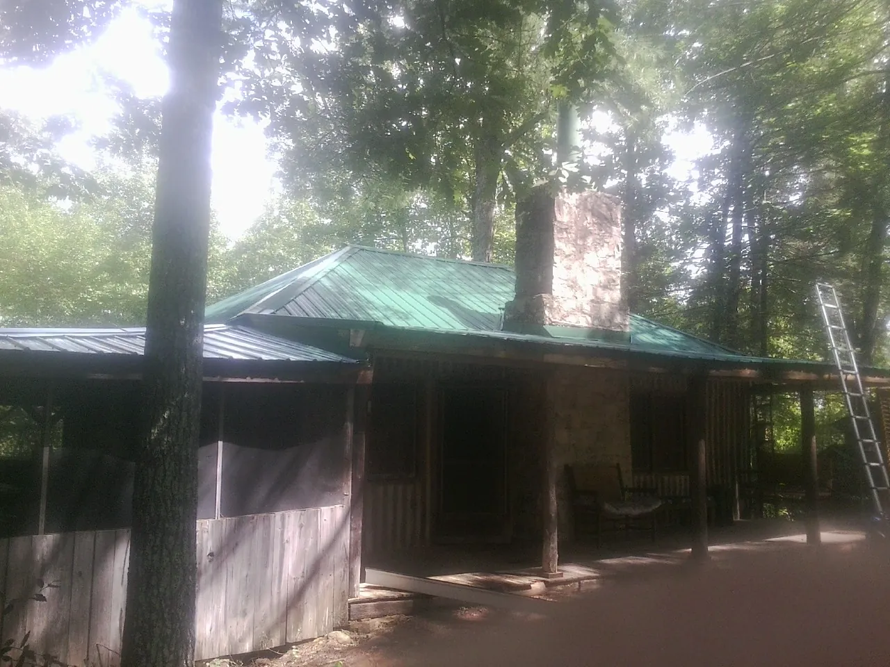 Green metal roof and stone chimney above a log cabin porch in Brodhead