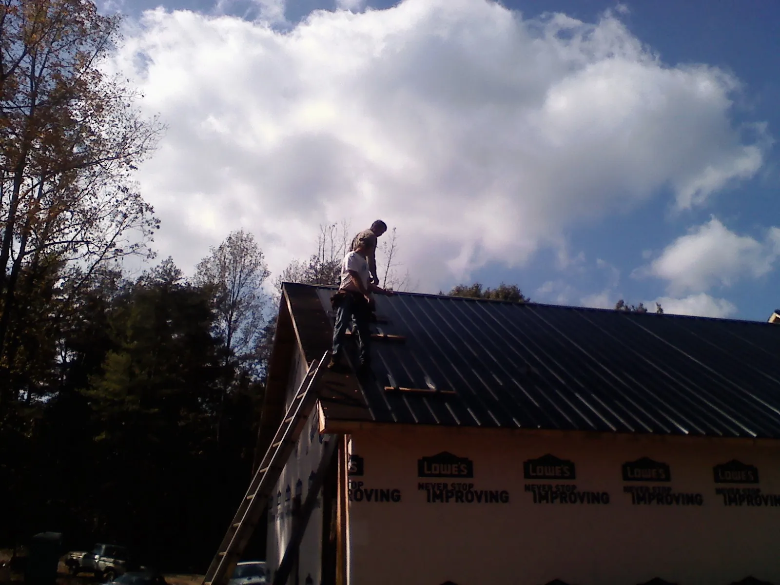 Roofer fastening dark metal panels high against a cloudy sky, from a Roof Inspection job in Brodhead