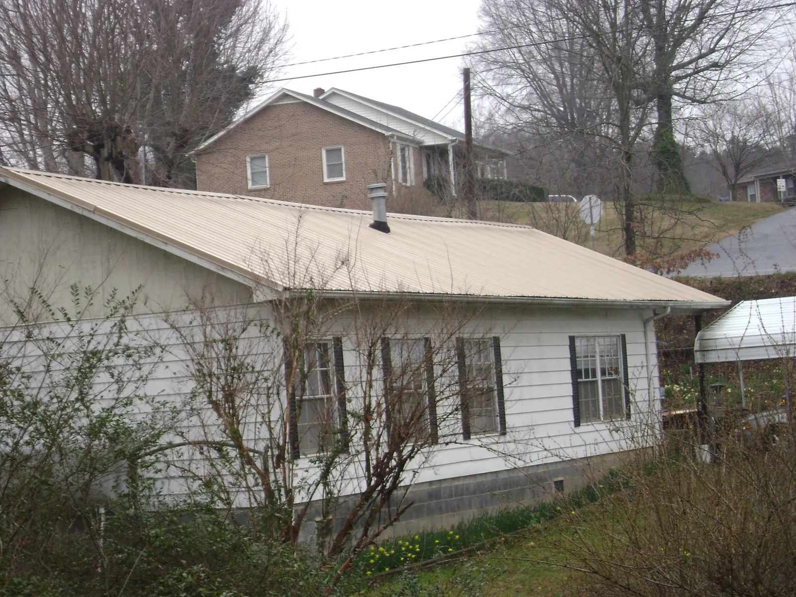 Tan metal roof on a white sided house set into a hillside — Commercial Roofing by Roofing Brothers in Brodhead